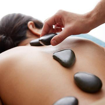 Warme massagestenen worden op de rug van een vrouw gelegd om vervolgens van start te gaan met de Hotstone Massage.