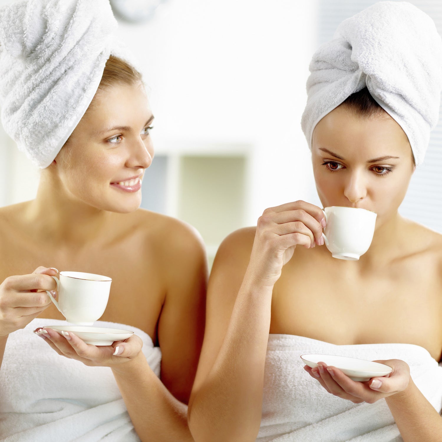 Twee vrouwen drinken gezellig een kopje koffie tijdens onze Girls’ Party. Zowel hun lichaam als haren zijn gewikkeld in een handdoek.